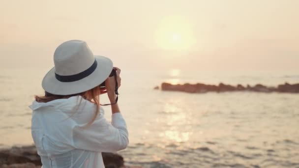 Mujer en sombrero tomando fotos de increíble puesta de sol sobre el mar — Vídeos de Stock