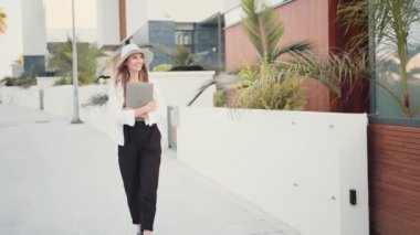 Güzel bir kadın caddede yürüyor ve dizüstü bilgisayar taşıyor.