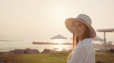 Şapkalı kadın deniz kenarında duruyor ve güzel manzaranın tadını çıkarıyor.