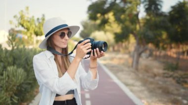 Moda görünümlü, dışarıda kameralı, zarif bir şapka takan oldukça havalı genç bir bayan model. Fotoğraf makinesi olan mutlu, heyecanlı, genç bir kadın fotoğrafçının fotoğrafı.
