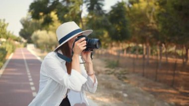 Mutlu genç kadın yürürken fotoğraf çekmek için modern dijital kamera kullanıyor. Yazlık şapkalı ve elbiseli bir kadın turist geziden kalan anıları saklıyor. Genç kadın fotoğrafçı gezgin