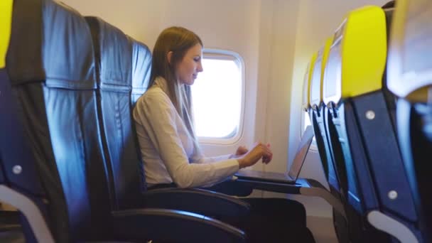 Mujer de negocios cansado de tomar siesta después del trabajo en el portátil inalámbrico mientras vuela en avión. Mujer caucásica sentada cerca de la ventana y frotándose los ojos. Concepto de personas, exceso de trabajo y tecnología. — Vídeos de Stock