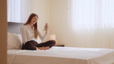 Otel odasındaki video görüşmesi için akıllı telefonu kullanan mutlu kadın.