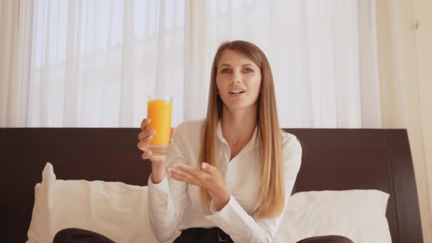 Жінка тримає склянку апельсинового соку і розмовляє на камеру — стокове відео
