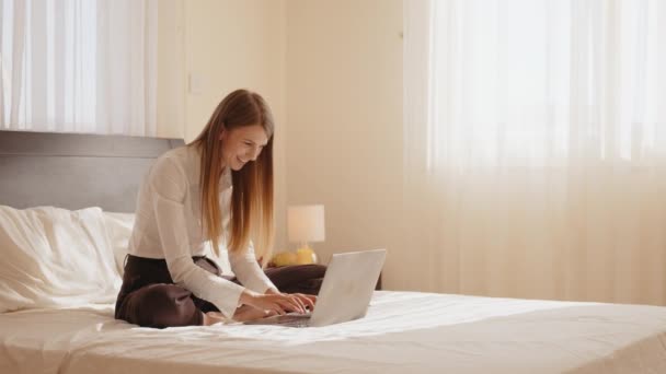 Leende kvinna sitter på sängen och använder modern bärbar dator — Stockvideo