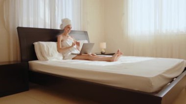 Banyo havlusundaki kadın otel odasındaki video görüşmesi için dizüstü bilgisayar kullanıyor.