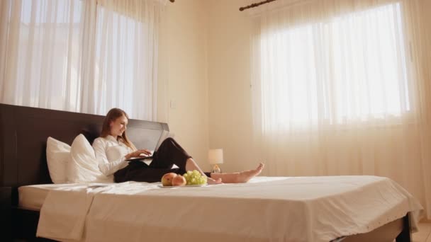 ベッドに横になって無線のノートパソコンに入力する女 — ストック動画