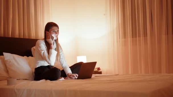 Mulher falando no celular enquanto sentado na cama com laptop — Vídeo de Stock