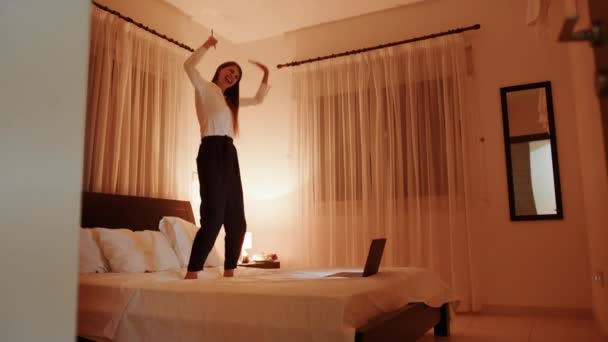 Happy woman jumping on bed with smartphone in hands — Stock Video