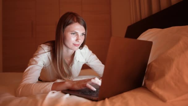 Kobieta leżąca na łóżku w godzinach wieczornych i korzystająca z laptopa — Wideo stockowe
