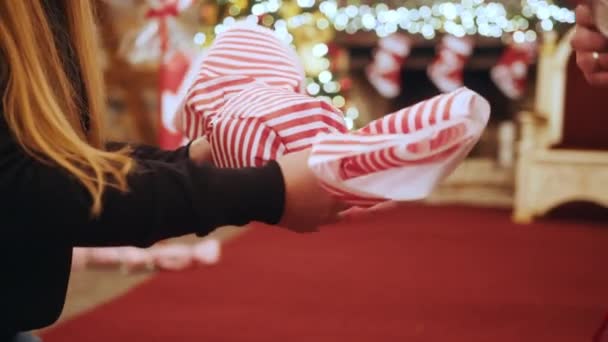 Detailní záběr ženské ruce dělat velké vánoční ozdoby v podobě cukroví ve vánočním obchodě nebo domě. V pozadí je krb zdoben vánočními světly a ponožkami — Stock video