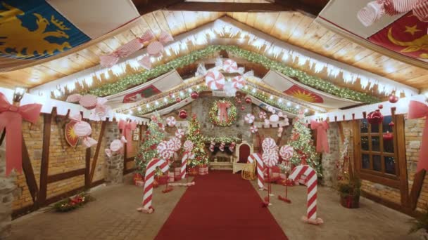 Casa di Natale grande di Babbo Natale, un sacco di alberi di Natale e caramelle. La casa di Natale è decorata con luci. Albero di Natale con decorazioni e regali vicino a un camino con luci — Video Stock