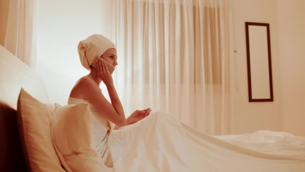 Banyodaki kadın yatakta uzanıyor ve cep telefonuyla konuşuyor. — Stok video