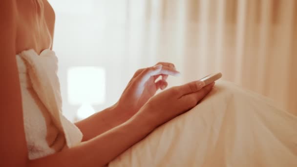 Yatakta uzanan ve akıllı telefondan yazı yazan bir kadın. — Stok video