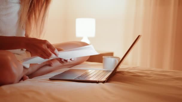 Frau liest Dokumente und tippt im Bett auf Laptop — Stockvideo