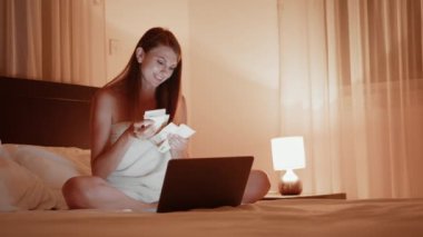 Yatakta dizüstü bilgisayarı olan ve para sayan bir kadın.