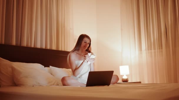 Fröhliche Frau zählt Bargeld, während sie Laptop auf dem Bett benutzt — Stockvideo