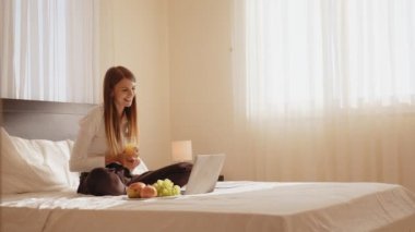 Çekici genç bir kadın rahat bir yatakta dinleniyor ve video görüşmesi için kablosuz bilgisayarı kullanıyor. Otel odasında internet üzerinden iletişim kuran bir kadın yolcu. Dizüstü bilgisayara bakıp yatakta duygusal hareketler yapan bir kadın.