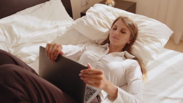 Young woman on the bed typing and working on a laptop, distance learning. Freelancer, distant work, work at home, online education. Self isolation. Portrait of beautiful young woman with laptop on bed — Stock Video