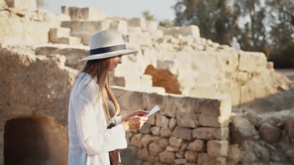 Женщина в летней шляпе ходит среди разрушенного древнего храма — стоковое видео