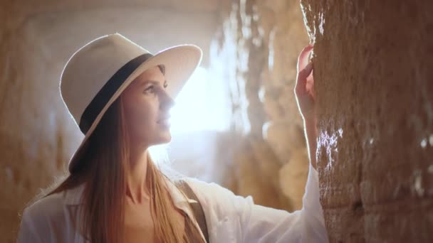 Жінка стоїть всередині стародавнього храму і торкається стіни — стокове відео