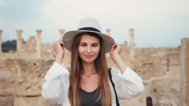 Женщина в летней шляпе смотрит в камеру среди старого храма — стоковое видео