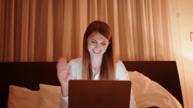 Gülümseyen esmer kız, akşam odasında web kamerasından görüntülü arama yapıyor. Mutlu kadının gece evde dizüstü bilgisayarında görüntülü sohbet etmesi. Genç bir kadının portresi internette kanepede sohbet ediyor..