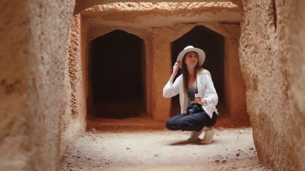 Jeune femme caucasienne accroupie avec smartphone et appareil photo numérique parmi les ruines de l'ancien temple. Examen des vieux bâtiments historiques avec des gadgets modernes. Femme tout en examinant temple antique — Video