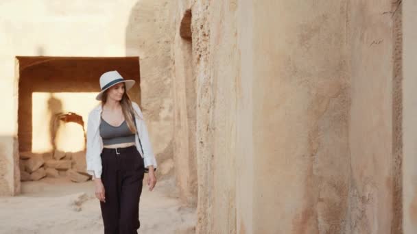 Competent female archeologist in white summer hat walking among ancient building with digital camera on neck. Concept of people, science and history. Focused woman examining ruins of ancient temple — Stockvideo