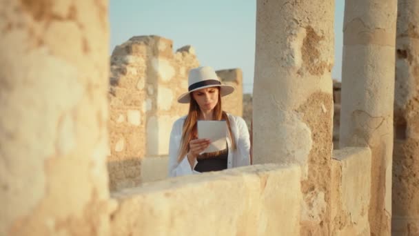 Цікава біла жінка в літньому капелюсі і повсякденному вбранні використовує карту при вивченні історичних будівель. Археологічні експедиції та дослідники. Жінка в капелюсі вивчення історичних будівель — стокове відео