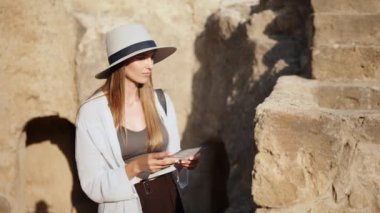 Beyaz şapkalı beyaz kadın arkeologun portresi dışarıda dururken gülümsüyor ve kameraya bakıyor. Eski tapınağın bulanık arka planı. Antik tapınaktaki kadın arkeolog.