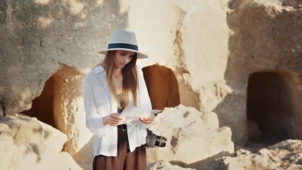 Femme blanche en chapeau d'été et lunettes de soleil examinant les colonnes antiques. Archéologue professionnel avec papiers et appareil photo à la découverte de nouveaux endroits avec des ruines. Touriste fille avec appareil photo et ordinateur portable. — Video