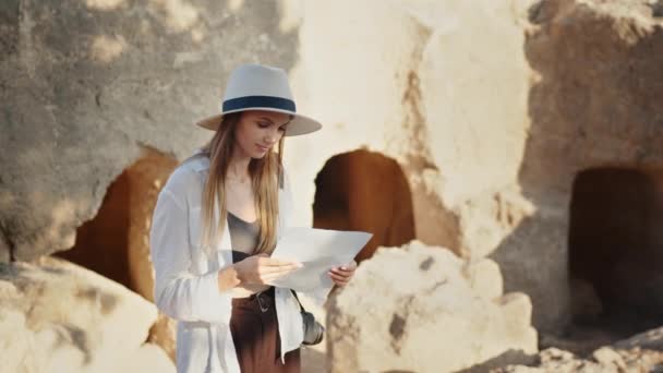 Mujer retrato en sombrero de verano y gafas de sol examinando columnas antiguas. Arqueólogo profesional con papeles y cámara fotográfica descubriendo nuevos lugares con ruinas. Chica turista con cámara y portátil — Vídeos de Stock