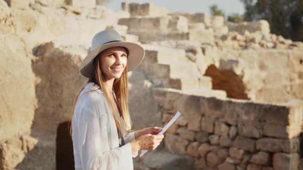 Egy fiatal nő kezében néhány papírral és fényképezőgéppel a vállán. Portré nő, ősi oszlopokat vizsgál. Szakmai archeológus fényképezőgép felfedezni az új helyeket romok. — Stock videók