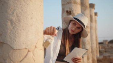 Antik tapınağın kalıntıları arasında duran bir arkeolog. Kazı için fırça tutan ve elinde harita tutan bir kadın. Sütunları olan eski bir tapınakta haritaya bakan bir kız. Arkeolojik Kazı Alanı