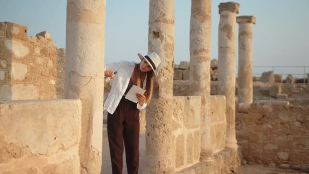 Bevoegde vrouwelijke archeoloog die tussen ruïnes van oude tempel staat. Vrouw met borstel voor graven en kaart in handen. Meisje toerist In een oeroude tempel met zuilen kijkend naar de verslagen van een kaart. — Stockvideo