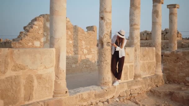 Competente arqueóloga femenina de pie entre las ruinas del antiguo templo. Mujer sosteniendo cepillo para cavar y mapa en las manos. Chica Turista En un antiguo templo con columnas mirando los registros de un mapa. — Vídeo de stock