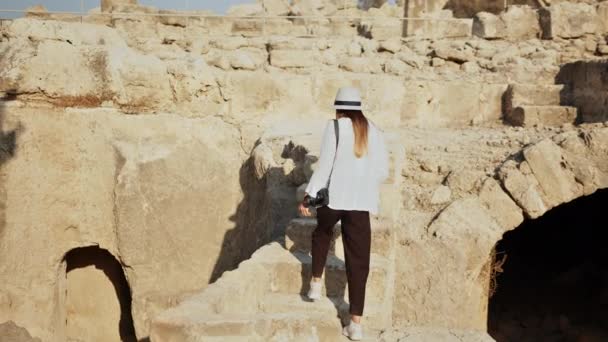 在古建筑的废墟中，身着休闲装、头戴白帽的高加索女人的倒影。考古和遗产的概念。戴着夏帽的女人走在古建筑的废墟中. — 图库视频影像