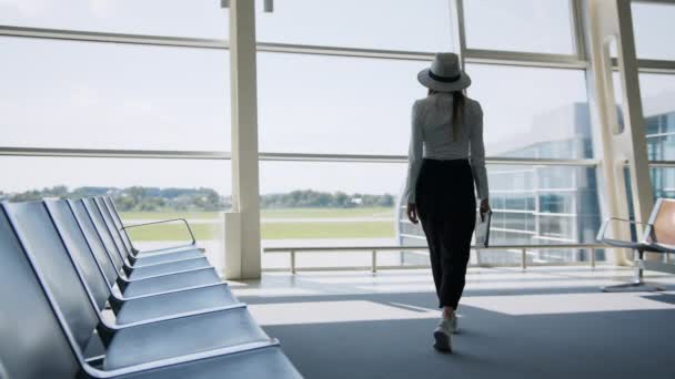 Menina turista freelancer trabalha e espera voo na sala de espera. Viagens conceituais, trabalho remoto. Silhueta no fundo de uma grande janela. O conceito de trabalho remotamente do escritório — Vídeo de Stock