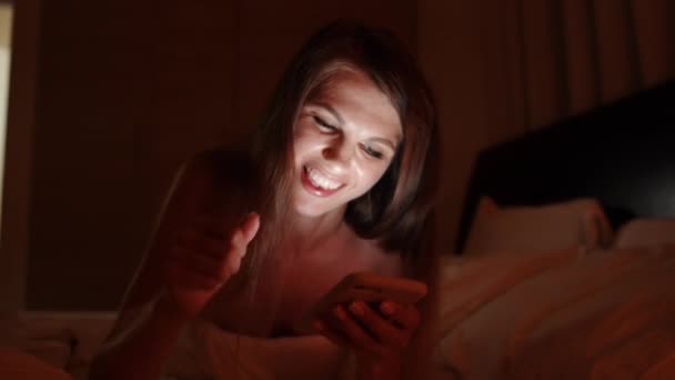 Wanita muda yang cantik menggunakan ponsel pintar di bawah selimut di kamar tidur saat tidur. Wanita menggunakan telepon pintar dan berbaring di ranjang saat malam. Orang-orang, waktu tidur dan konsep istirahat wanita muda di tempat tidur dengan smartphone — Stok Video