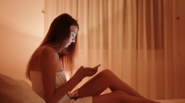 Akıllı telefondan oynayan bir kadın. Kadın heyecanlı hissediyor bilardo galibiyetini kutlarken akıllı telefona bakarak, heyecanlı kız bağırarak evet diyor cep telefonuyla oyun uygulaması kazanıyor evde yatakta oturuyor.