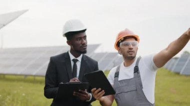 Elinde tabletle Afro-Amerikan müfettişi Hintli teknisyene güneş enerjisi üzerine çalışma talimatı veriyor. Ekoloji projesi ve alternatif enerji konsepti. Güneş panelleri hakkında konuşan teknisyen