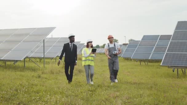 Trabajadores caminando en la estación solar. Vista de dos inspectores en cascos blancos caminando sobre estación solar con técnico en uniforme. Ingenieros multirraciales examinan el trabajo de las células fotovoltaicas al aire libre. — Vídeos de Stock