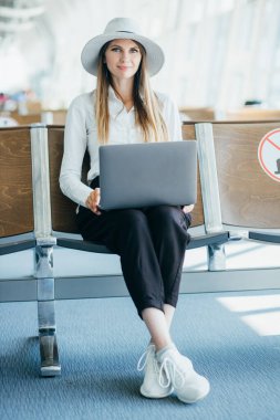 Uçuş için beklerken onu laptop çalışma genç şık iş kadını ile Uluslararası Havaalanı terminal, el bagajı