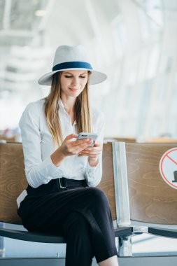 Sıradan bir genç kadın, kalkış kapısında uçağa binmek için beklerken cep telefonunu kullanıyor..