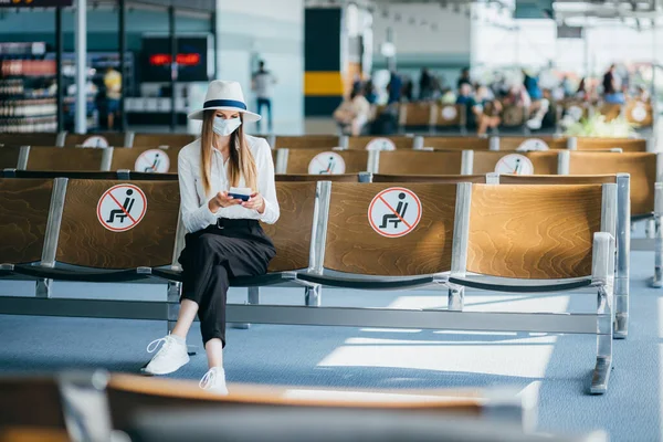 Kvinnelig turist med maske med flybilletter og sittende i en sosialt distansert stol på flyplassen under Coronavirus epidemien. Konsept av ny normalitet for lufttransport på grunn av pandemi – stockfoto