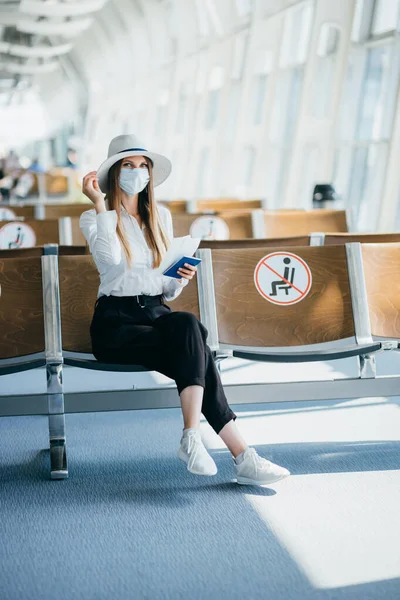 Turysta w masce siedzi w terminalu lotniska salon na pustych oznaczone krzesła na podstawie nowych normalnych i covid przepisów społecznych odległości. Kobieta siedząca w salonie na lotnisku i patrząca na jej paszport i podróże — Zdjęcie stockowe