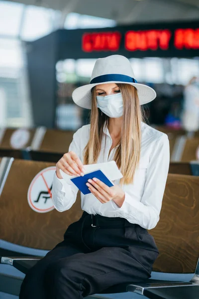 En ung reisende i medisinsk maske sitter på venteværelset med pass og billett. Reisekonsept under COVID 19-epidemien – stockfoto