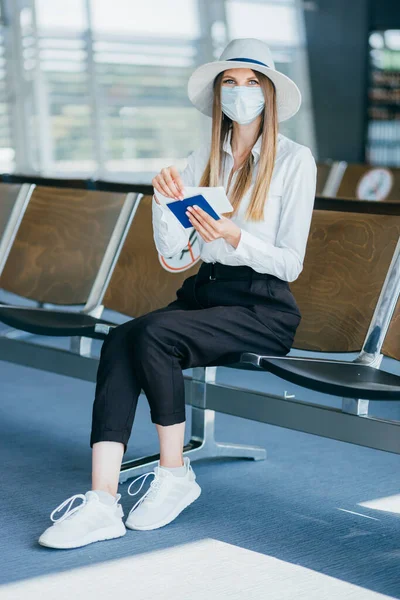 ผู้หญิงสาวที่มีหน้ากาก, พาสปอร์ตและตั๋วตรวจสอบตารางการเดินทางที่สนามบินนานาชาติหรือสถานีรถไฟ. แนวคิดการเดินทางในช่วงเวลาของการระบาด 19 โลภ . — ภาพถ่ายสต็อก