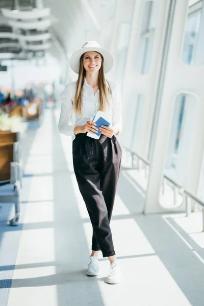Młoda dziewczyna, bizneswoman stojąca przy oknie na nowoczesnym lotnisku z biletem i telefonem, patrząca w kamerę. Portret pięknej dziewczyny w masce. Podróż służbowa samolotem. — Zdjęcie stockowe